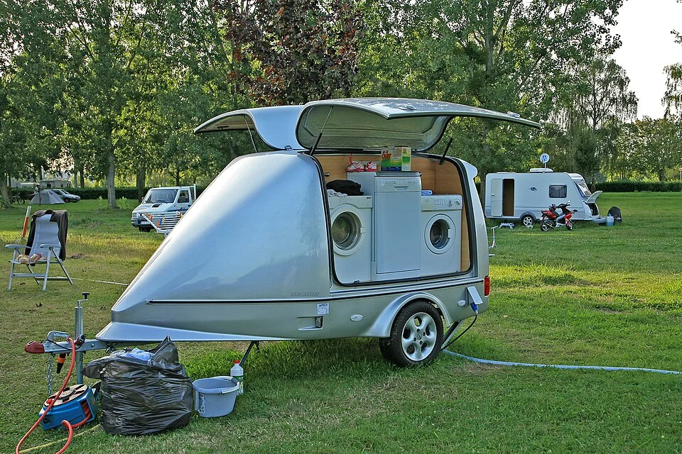 Een kleine caravan op een groene kampeerplaats